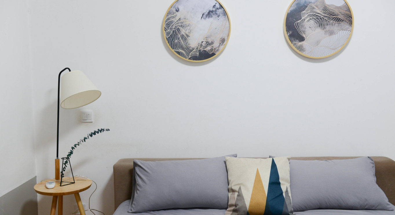 Space and organization with Feng Shui: A sofa with light-colored cushions, a lamp on the left, and round paintings on the wall.