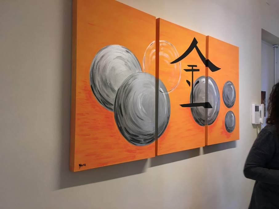 A tripartite Asian artwork with an orange background, featuring a large Chinese ideogram in the center and gray spheres surrounding it.