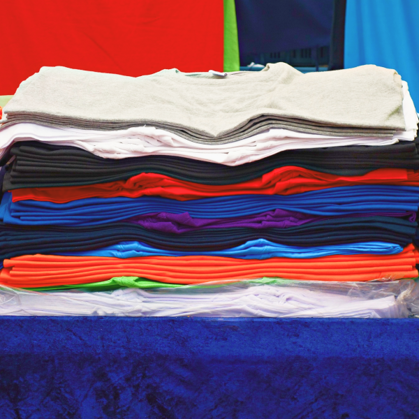 Many t-shirts in various colors, folded and stacked on top of each other.