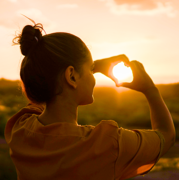 A girl forms a heart shape with her hands in front of a sunset. Ba Zi has guided her to make the right choices along her life path