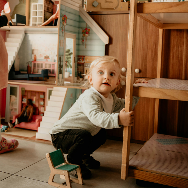 A child is playing in their room with a wooden dollhouse.