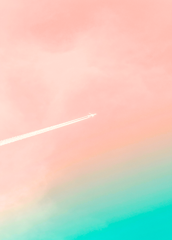 A white airplane flies in the distance against a sky of light pink and aquamarine.