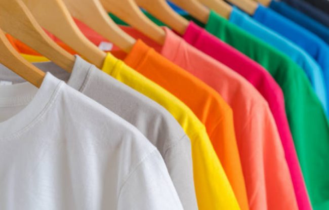 A lot of shirts of different colors hanging on wooden hangers.