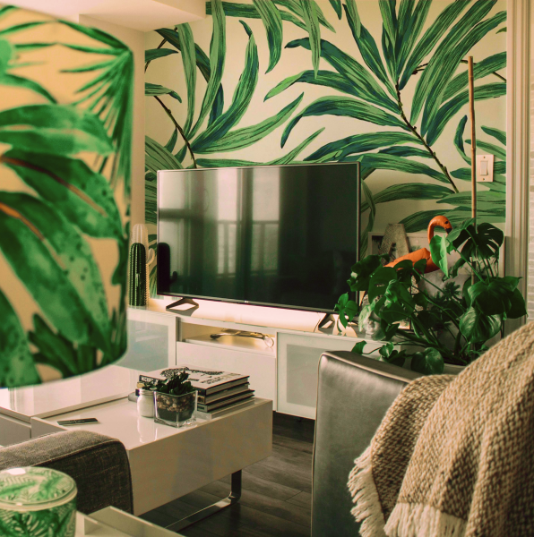 Cozy living room with a TV, decorated with vibrant plants. The wall behind the television features a print of a plant.