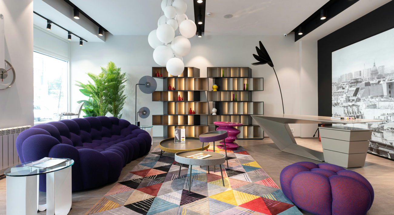 Modern room decor featuring a round-shaped purple sofa, a designer desk, and a multicolored rug. In Feng Shui, colors are essential.