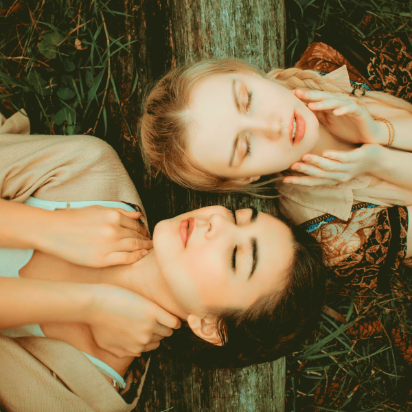 Two models with delicate features pose with their heads resting on a tree trunk in the midst of nature. Their eyes are closed as if they were resting.