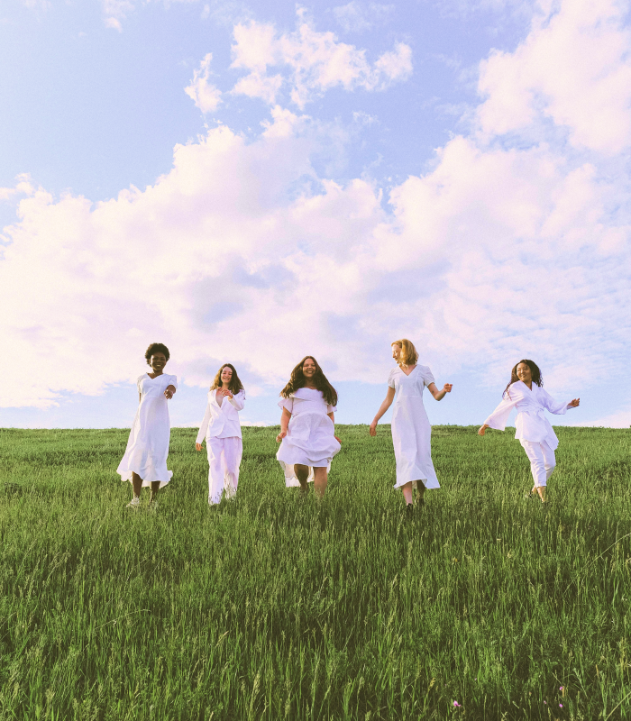 Naturopathy. Five women dressed in white smile as they walk along a path in a green meadow.