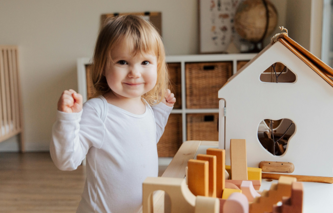 A little girl smiles happily while playing with her wooden playhouse.