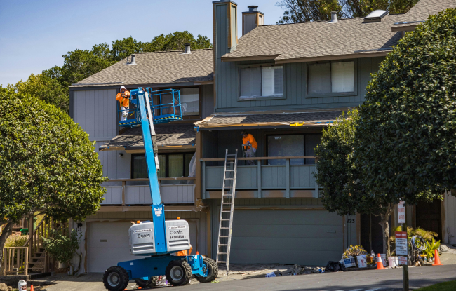 Workers in orange uniforms working on the exterior of a house renovation.