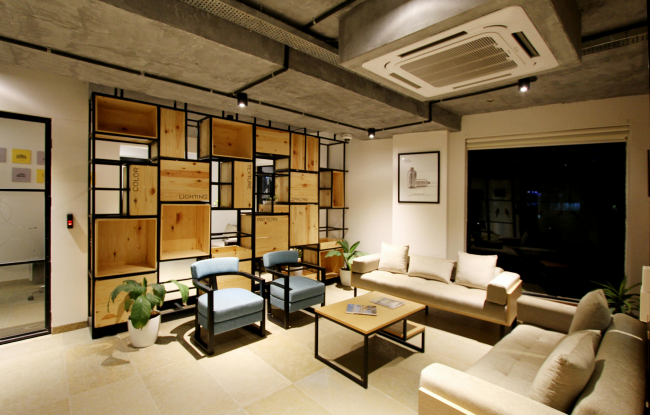 Open space with two cream-colored sofas and two blue chairs. Behind them is a wooden and metal structure.