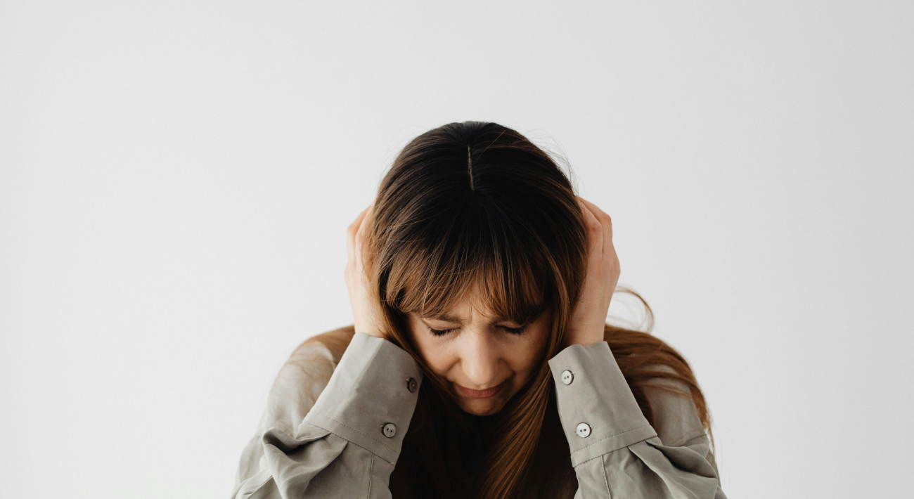 A woman covers her ears in the throes of inner pain.