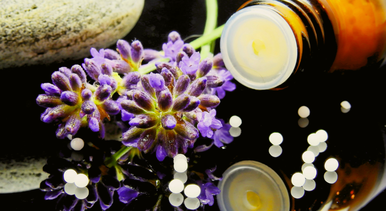 A small bottle containing Schüssler salts and some purple flowers on a glass table.