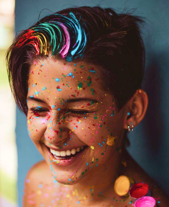 A girl with multi-colored hair and face paint, smiling playfully. Feng Shui and colors.