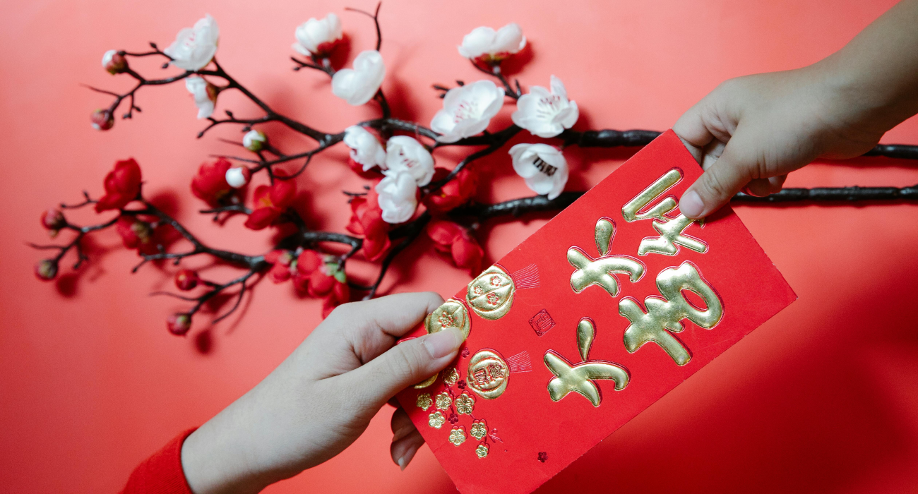 A pair of hands holding a red envelope with flowers in the background.