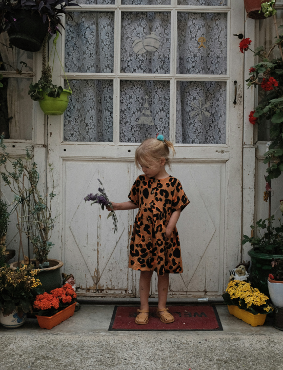 Girl in an orange and black dress holding a plant in front of her house door. Raffaela Marescalco's feng shui consultations will change your life.