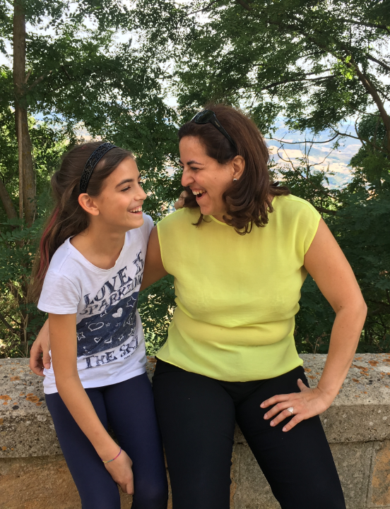 Raffaela Marescalco and her younger daughter Noemi are sitting on a low wall. They are smiling at each other. Both seem happy and are sharing a moment of closeness.