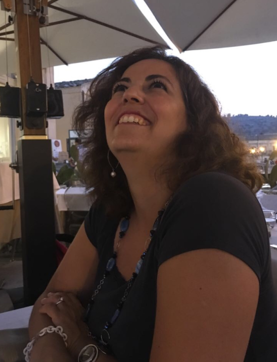 Raffaela Marescalco seated outdoors under a beach umbrella, looking upwards.
